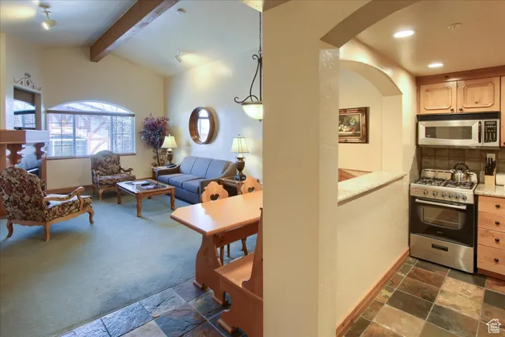 Kitchen featuring pendant lighting, backsplash, stainless steel appliances, lofted ceiling with beams, and light brown cabinetry
