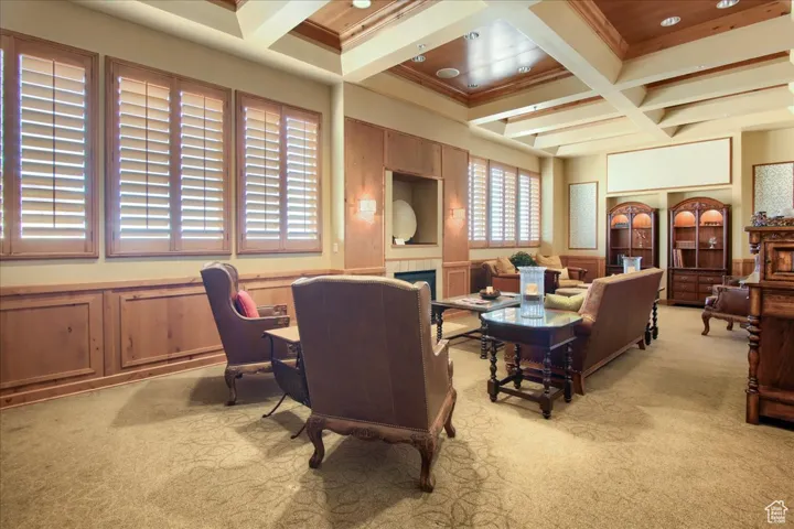 Interior space featuring a fireplace, beamed ceiling, coffered ceiling, light colored carpet, and crown molding