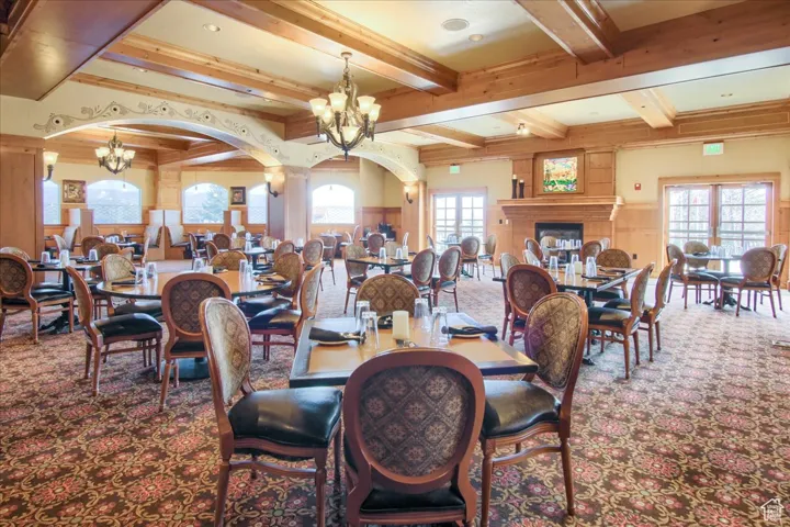 Carpeted dining space featuring a notable chandelier, a fireplace, and beamed ceiling