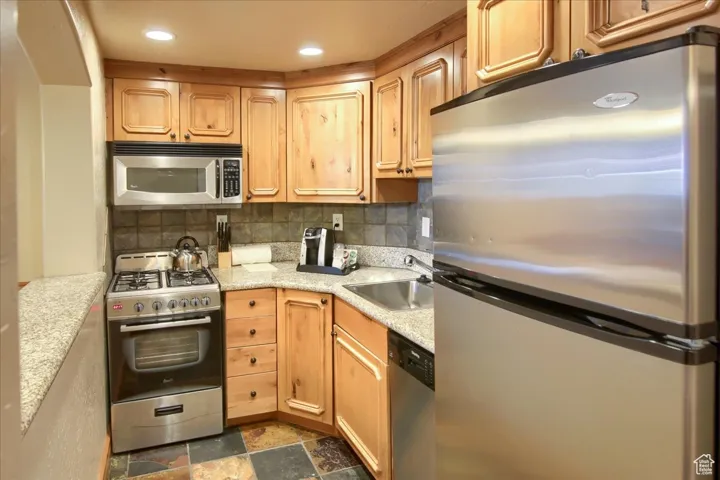 Kitchen with tasteful backsplash, sink, light stone counters, and appliances with stainless steel finishes