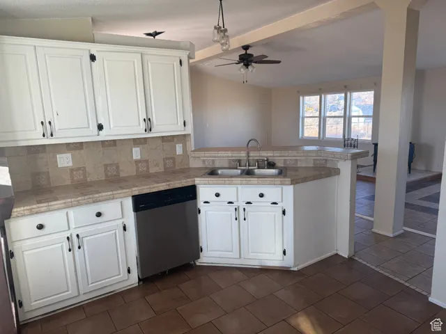 Kitchen featuring stainless steel dishwasher, kitchen peninsula, sink, and white cabinets