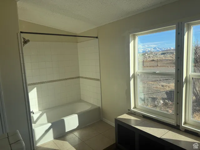 Bathroom featuring tile patterned flooring, a mountain view, tiled shower / bath combo, and a textured ceiling