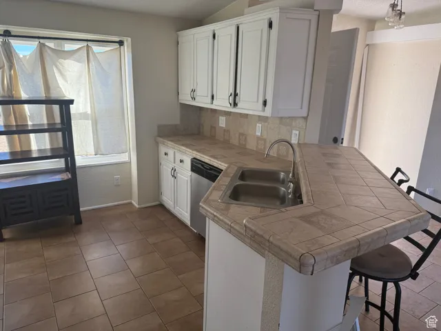 Kitchen with sink, a breakfast bar area, white cabinets, stainless steel dishwasher, and kitchen peninsula