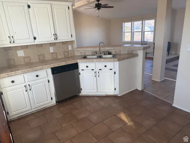 Kitchen with sink, stainless steel dishwasher, kitchen peninsula, white cabinets, and backsplash