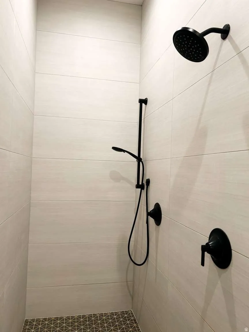 Shower enclosure featuring light-toned rectangular wall tiling, a geometric pattern mosaic floor, matte black rainfall showerhead, and a matching handheld shower with a wall-mounted control valve