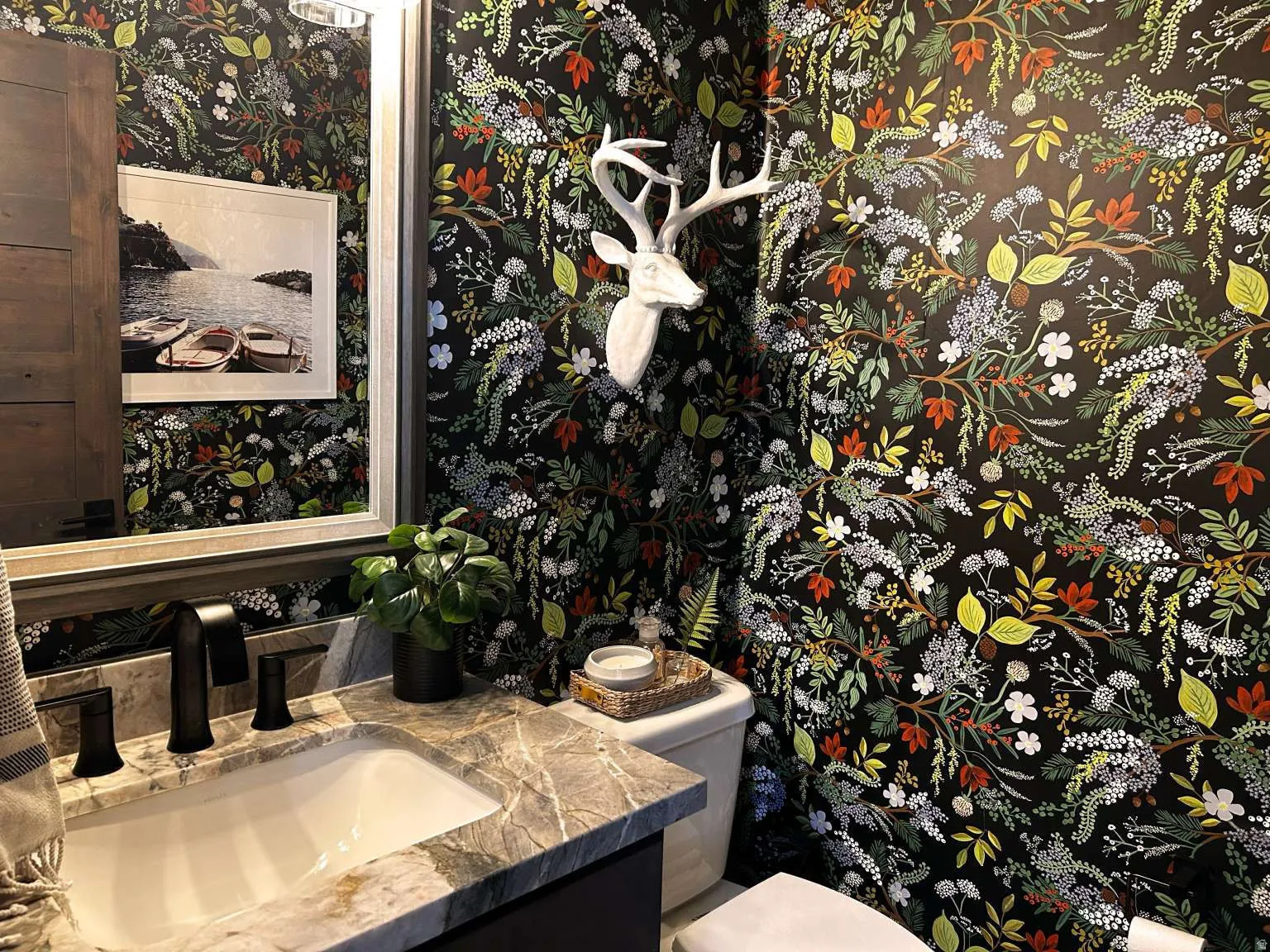 Powder room featuring botanical-patterned wall covering, a vanity with a stone countertop, an undermount sink, and a black faucet