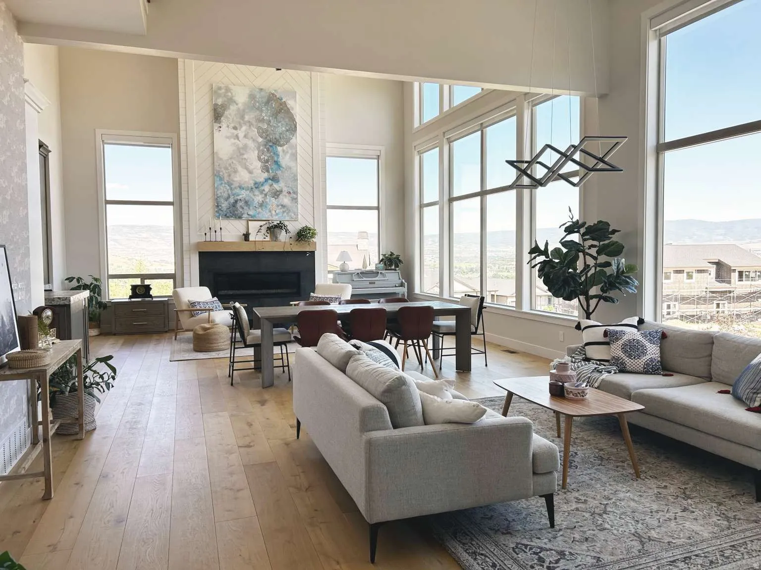 Open-concept living area featuring high ceilings with a statement chandelier, oversized windows, and light wood-finish flooring
