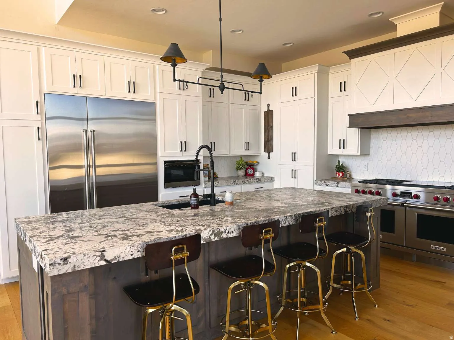 Spacious kitchen featuring a large central island with seating, a stainless steel refrigerator, white cabinetry with dark hardware, a professional-grade range, and a decorative hood