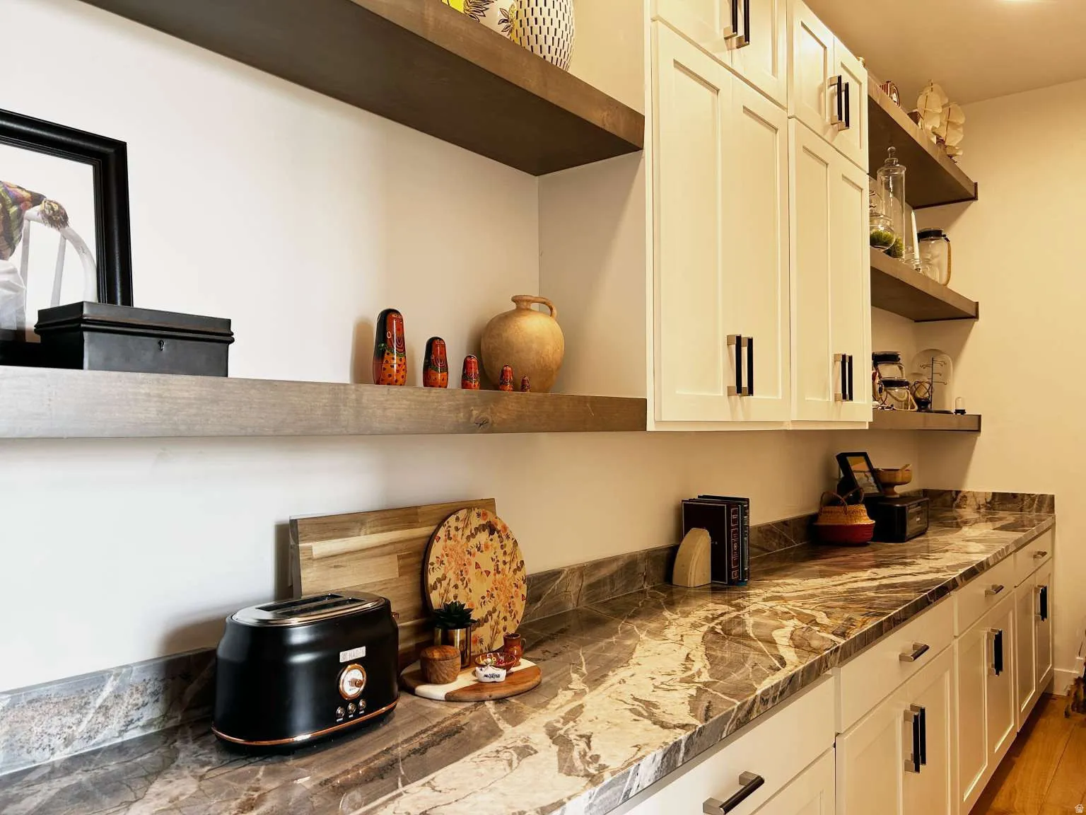 Kitchen or pantry area featuring patterned stone countertops, white shaker cabinetry with dark hardware, and multiple open wood-finish shelving units