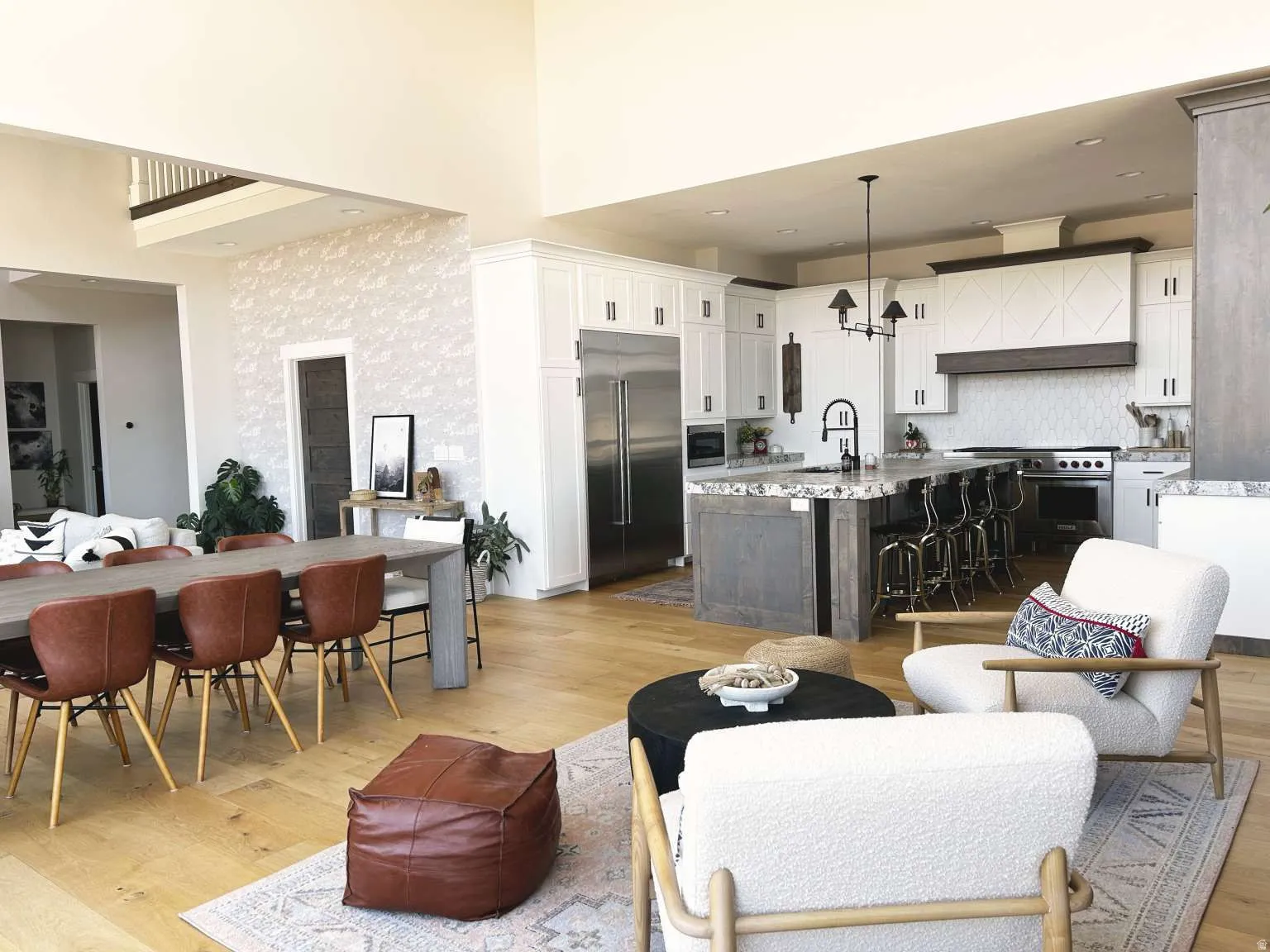 Open-concept kitchen and dining area featuring high ceilings, light wood-finish flooring, a kitchen island with seating, a stainless steel refrigerator, and white cabinetry