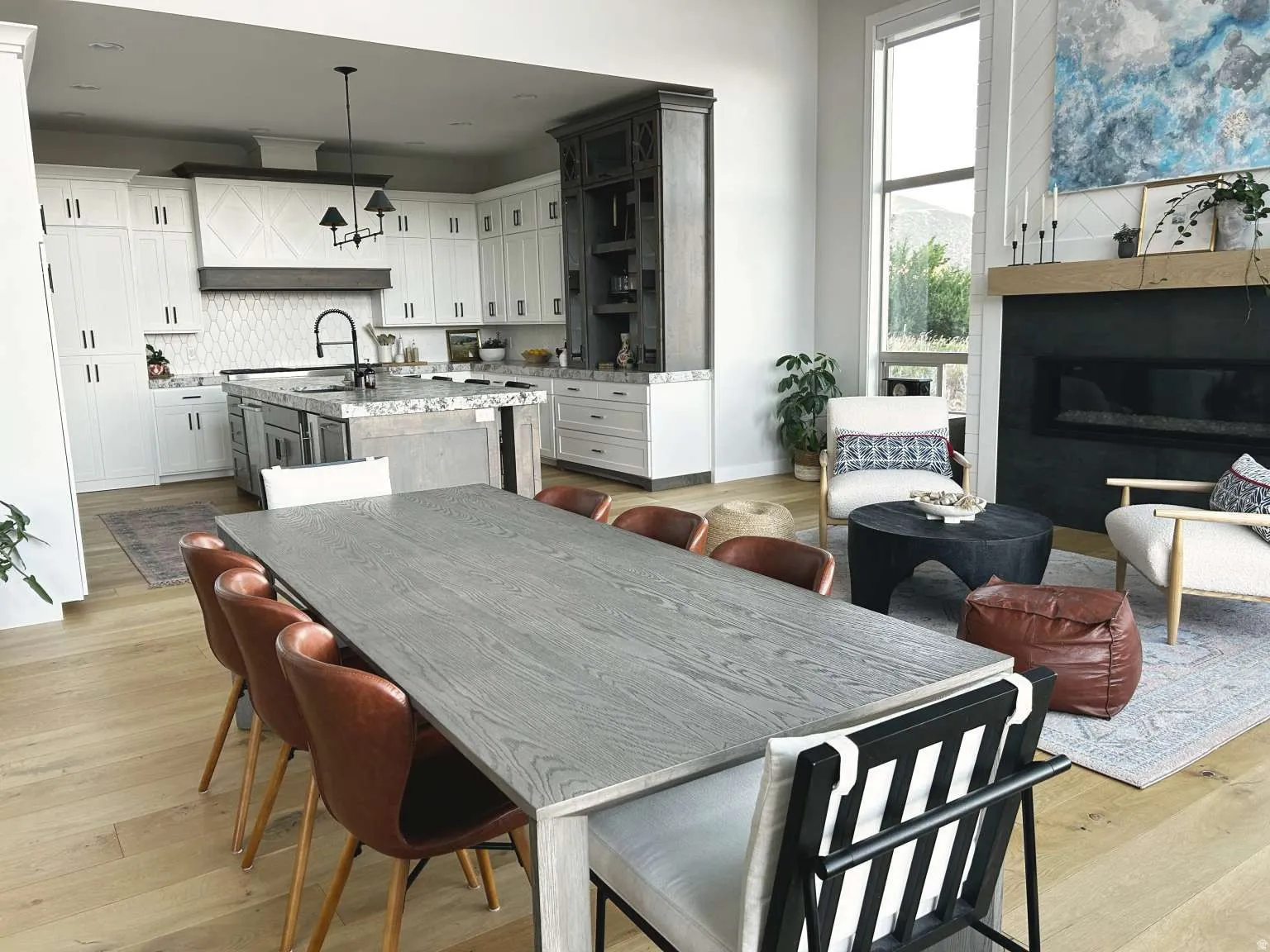 Open-concept living space featuring light wood-finish flooring, a contemporary linear fireplace with a dark surround, and a kitchen with white cabinetry and a central island
