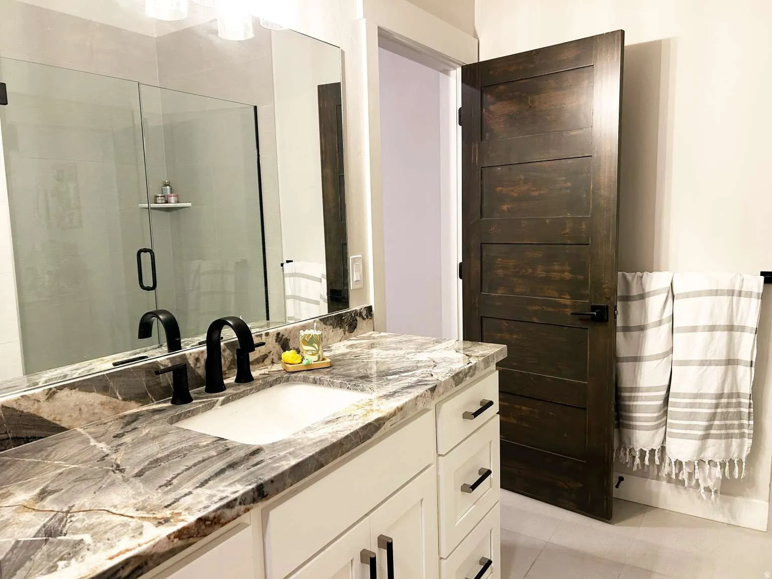 Bathroom featuring a white vanity with panel-front cabinetry, a stone countertop with a rectangular undermount sink, and a black two-handle faucet