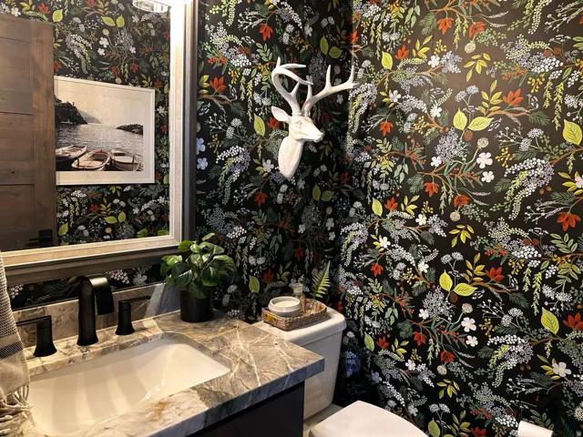 Powder room featuring botanical-patterned wall covering, a vanity with a stone countertop, an undermount sink, and a black faucet
