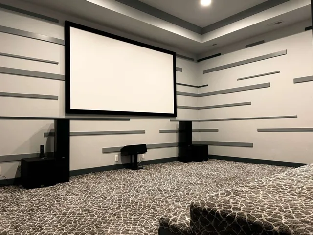 Dedicated media room featuring a large projection screen, textured wall paneling, recessed lighting, and patterned carpet flooring