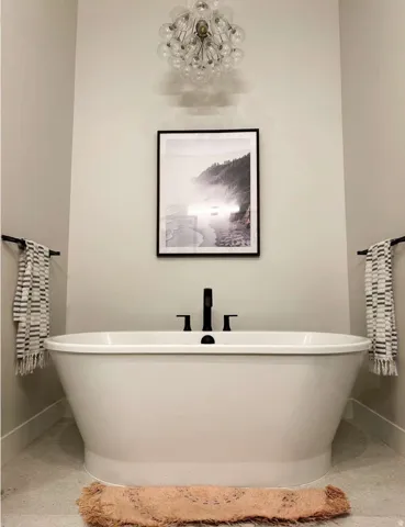 Freestanding soaking tub featuring matte black fixtures, an overhead globe chandelier, light-toned wall paint, and gray tile flooring
