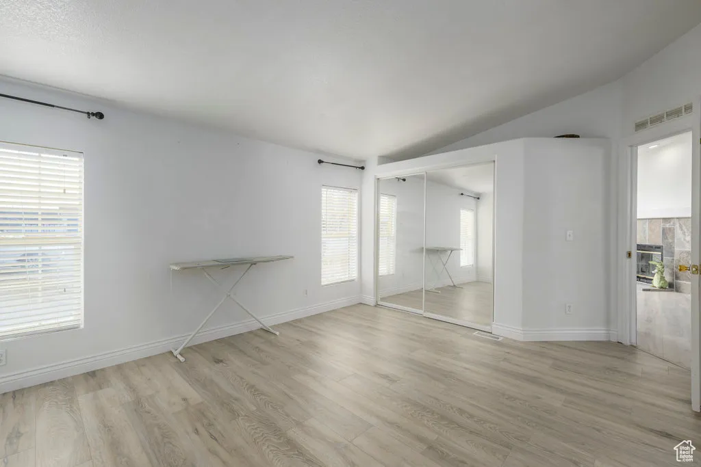 Unfurnished bedroom with baseboards, visible vents, lofted ceiling, and light wood-type flooring