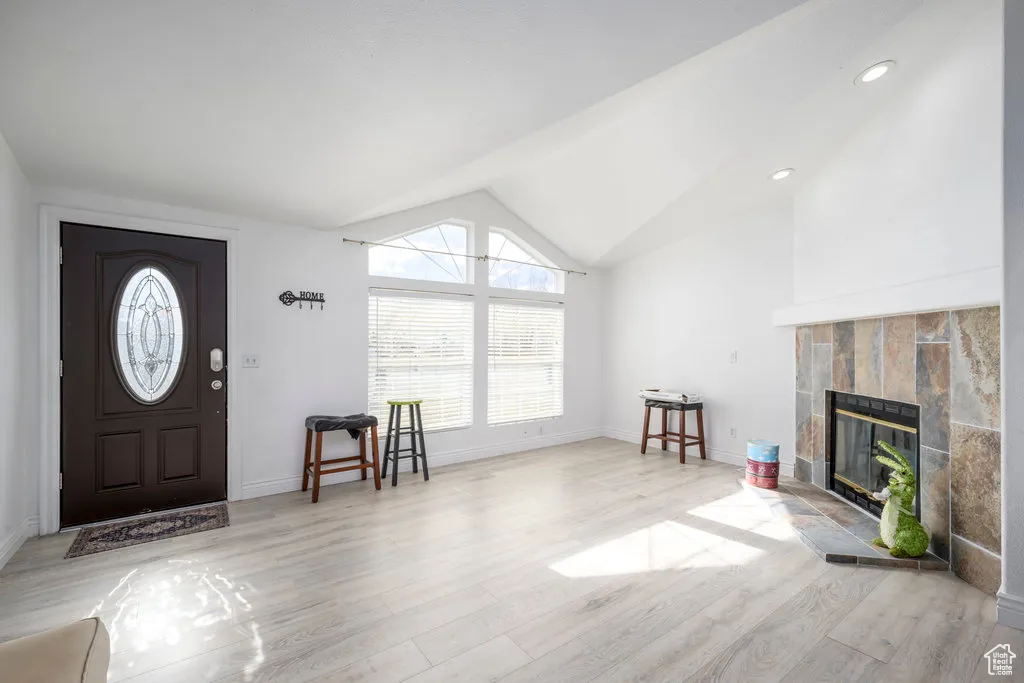 Entryway with baseboards, a tiled fireplace, light wood-style floors, lofted ceiling, and recessed lighting