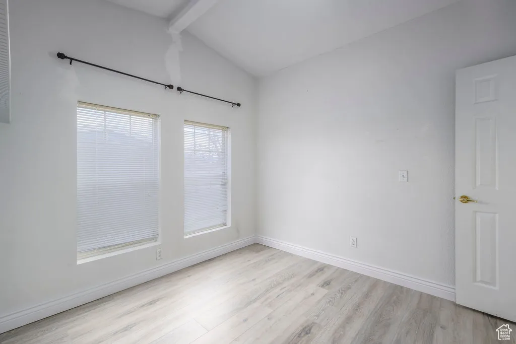 Empty room featuring light wood-style flooring, lofted ceiling with beams, and baseboards