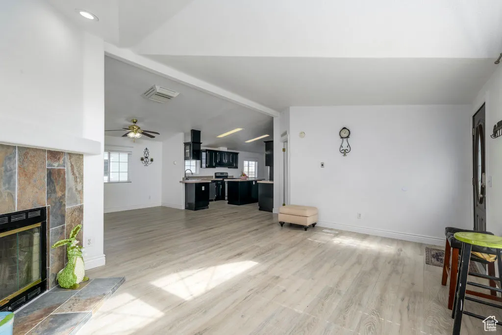 Living area with baseboards, a tile fireplace, light wood finished floors, and vaulted ceiling with beams