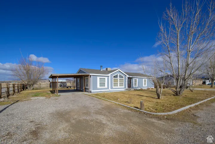 View of front of home featuring gravel driveway, a front yard, a carport, and fence