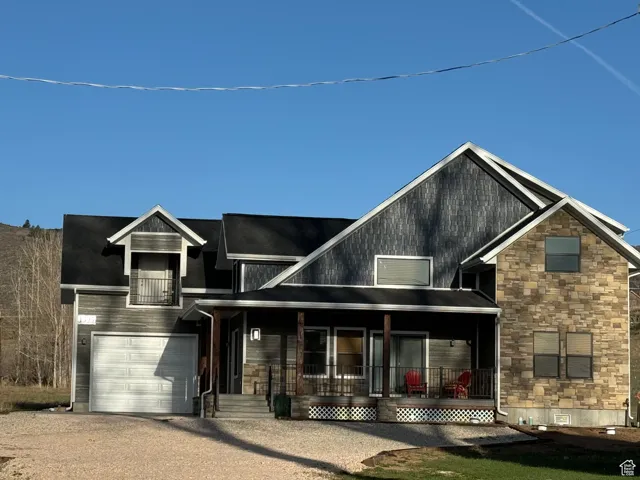 View of front of property with a garage, driveway, stone siding and a porch
