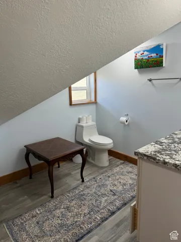 Bathroom with a textured ceiling, wood finished floors, toilet, and lofted ceiling