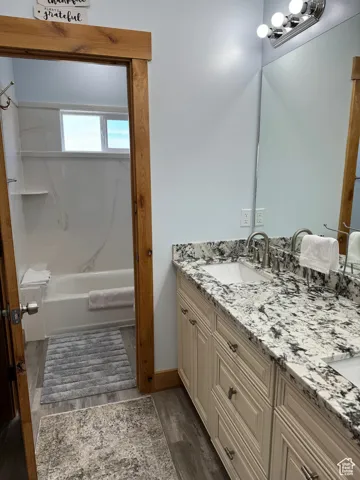 Primary Bathroom featuring double vanity, wood finished floors, tub / shower combination, and a sink