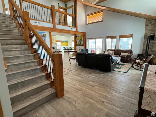 Living room with visible vents, a gas stove, wood finished floors, high vaulted ceiling, and stairs