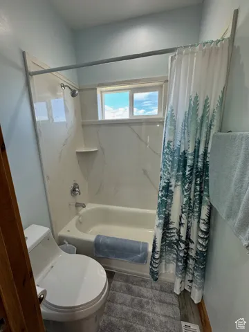 Full bath with shower / tub combo with curtain, toilet, and wood finished floors
