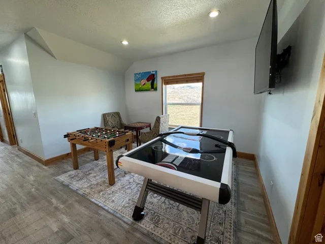 Rec room featuring lofted ceiling, a textured ceiling, wood finished floors, and baseboards