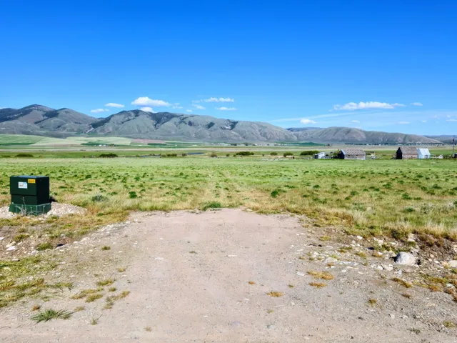 Expansive open land featuring a clear blue sky, distant mountains, and a verdant field