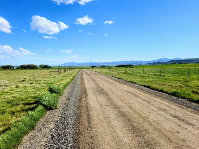 Expansive rural property featuring a gravel road, green pastures, and distant mountain peaks