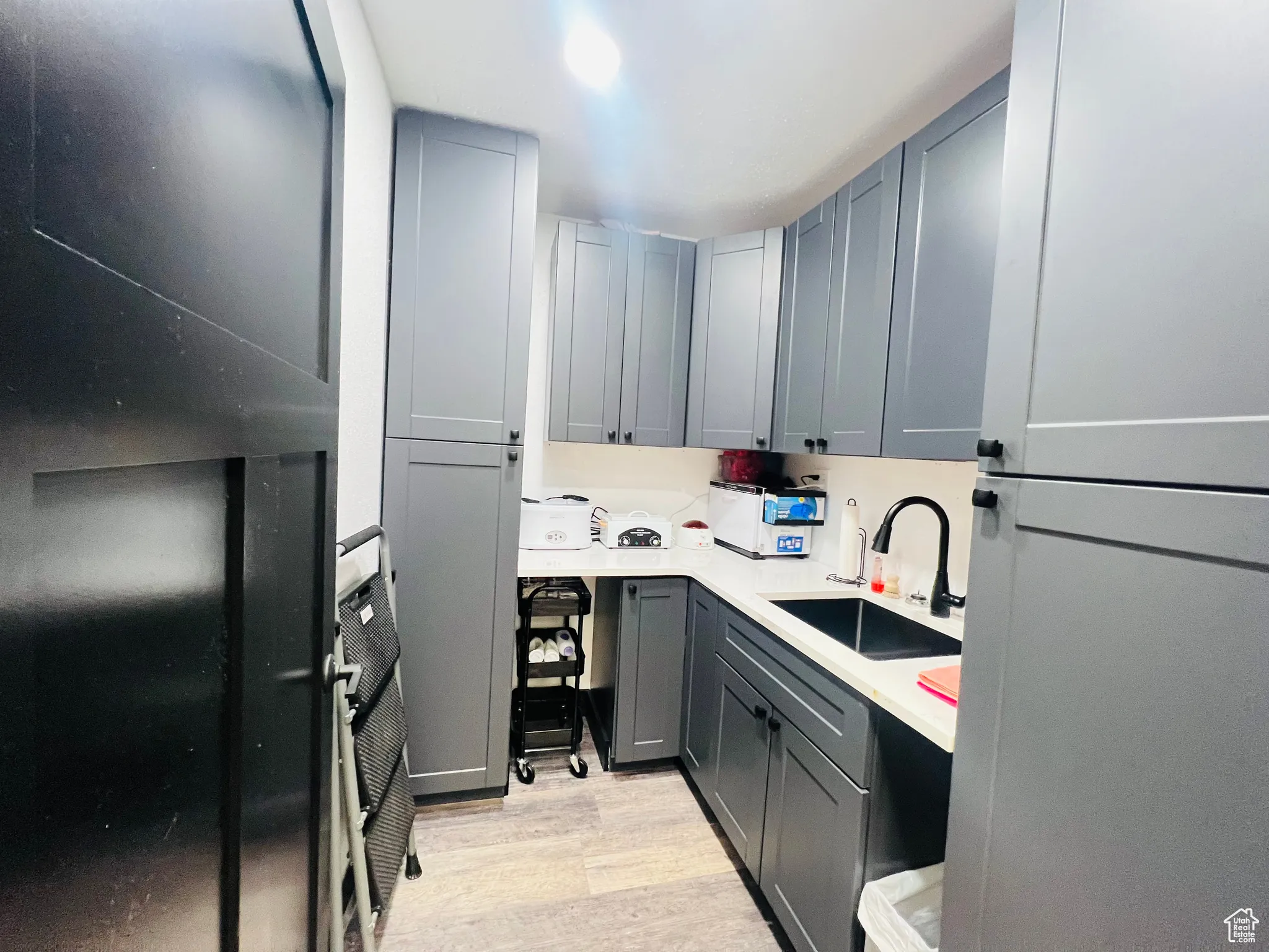 Kitchen featuring freestanding refrigerator, gray cabinets, light countertops, light wood-style floors, and a sink