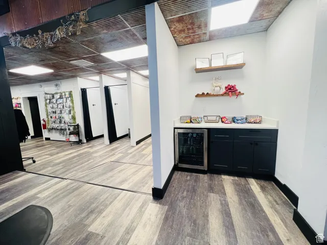Bar with beverage cooler, baseboards, a bar, and light wood finished floors