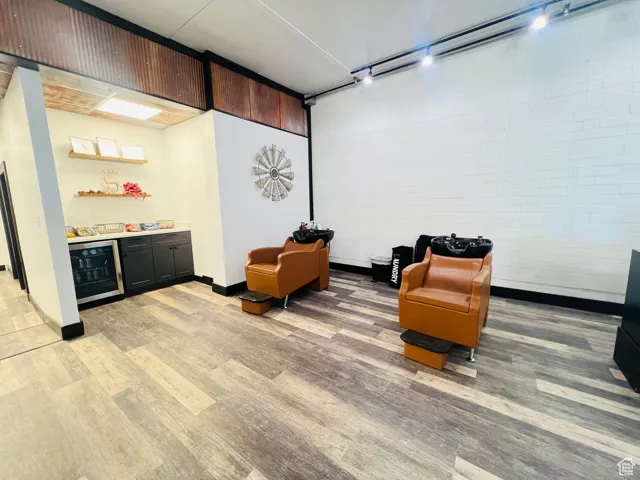 Sitting room featuring light wood finished floors, brick wall, wine cooler, rail lighting, and a bar