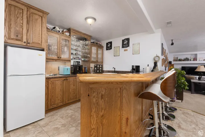 Kitchen with visible vents, brown cabinetry, glass insert cabinets, a breakfast bar area, and freestanding refrigerator