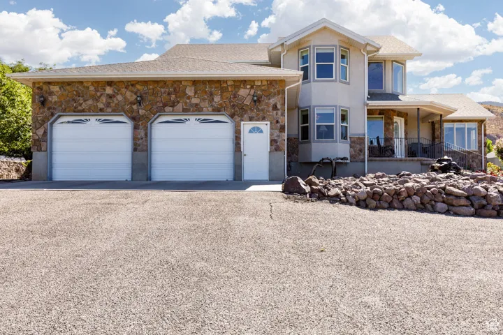 View of front of house featuring stone siding, driveway, a porch, an attached garage, and roof with shingles
