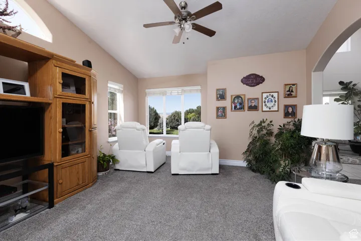 Living area with healthy amount of natural light, light carpet, vaulted ceiling, ceiling fan, and arched walkways