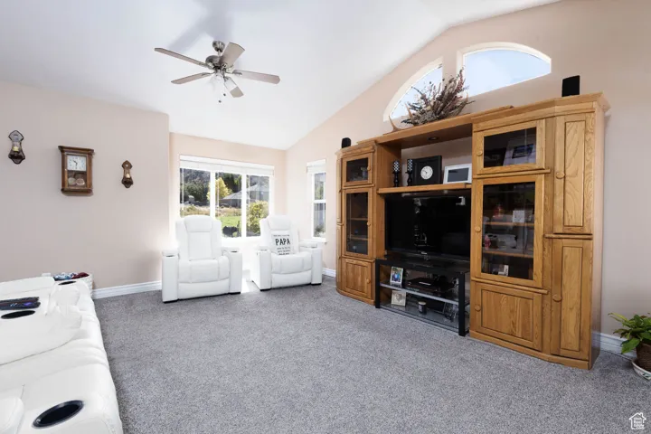 Living room featuring vaulted ceiling, light colored carpet, and ceiling fan