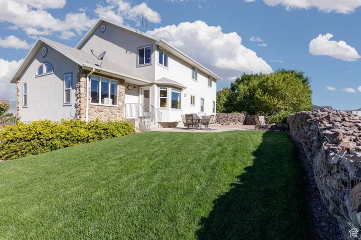 Rear view of property featuring a patio, stucco siding, stone siding, and a yard