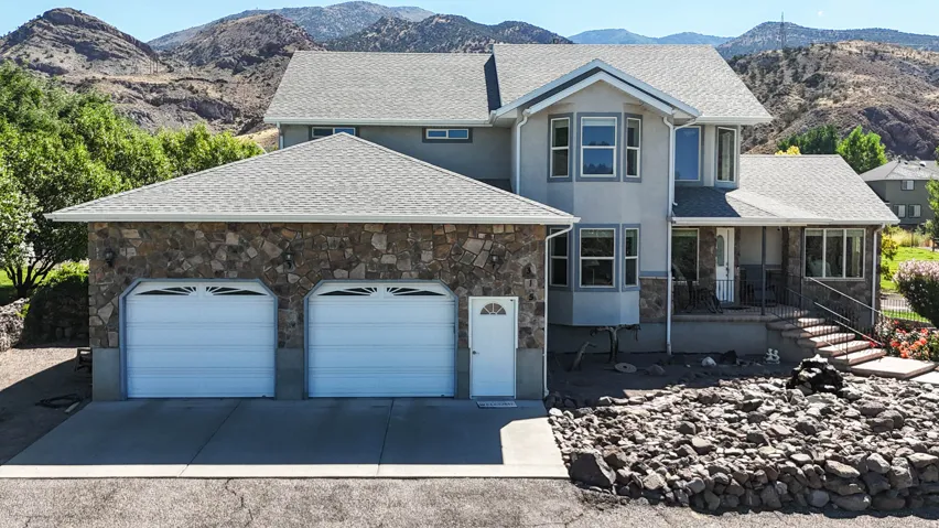 View of front facade with a mountain view, stone siding, a garage, concrete driveway, and roof with shingles