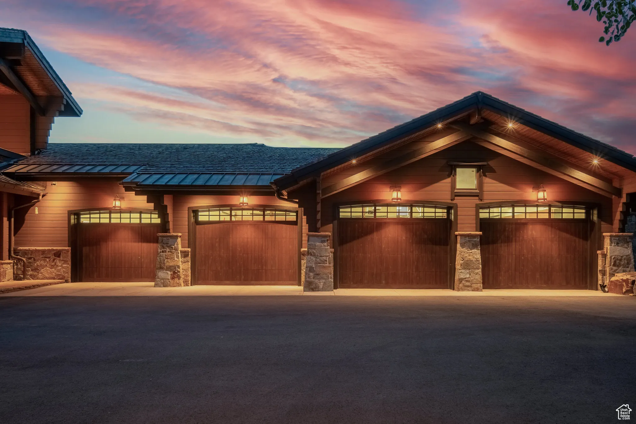 View of front of property featuring a standing seam roof, stone siding, asphalt driveway, a metal roof, and a garage