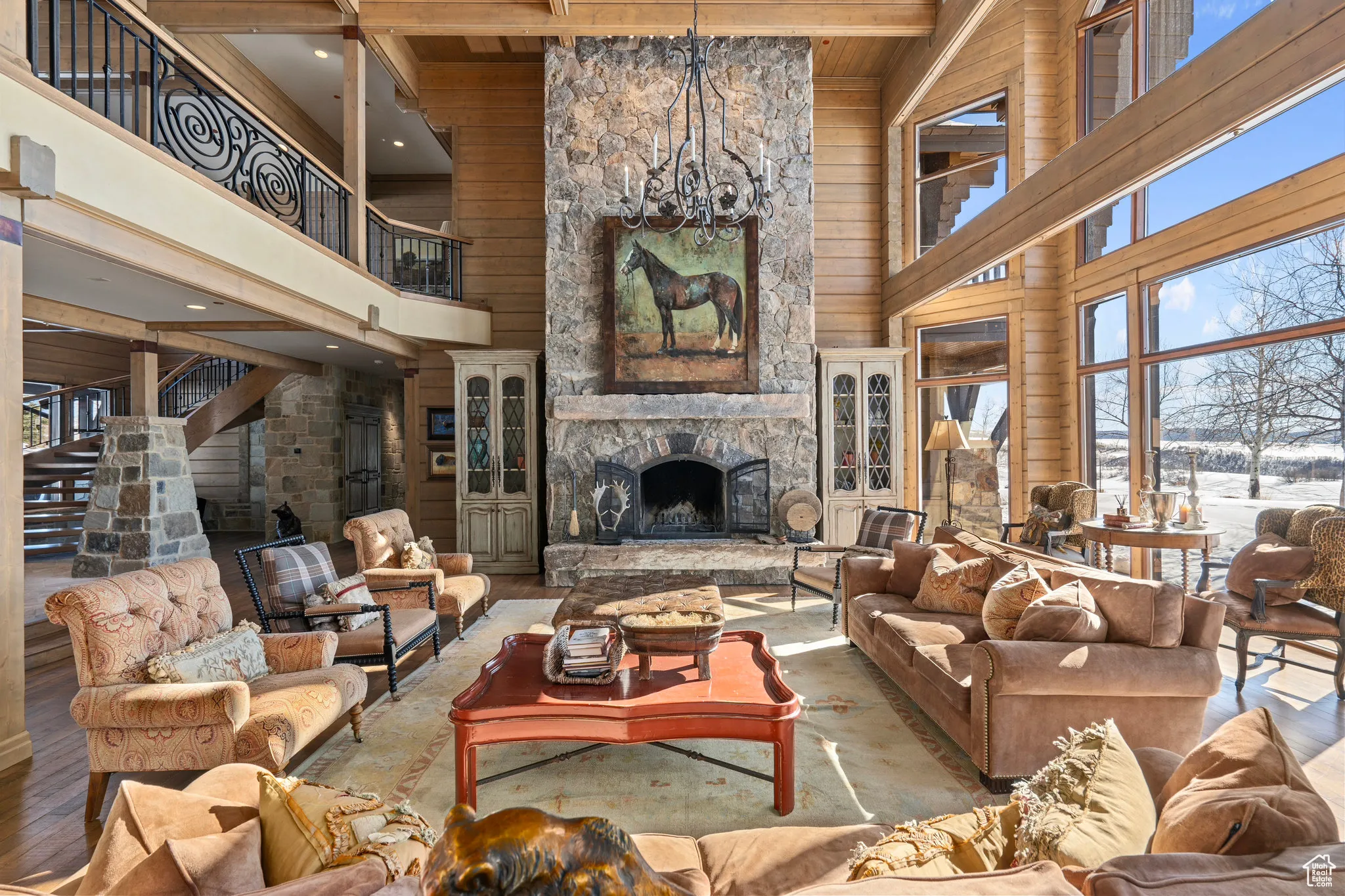 Living area featuring beamed ceiling, a high ceiling, a stone fireplace, wood walls, and a chandelier