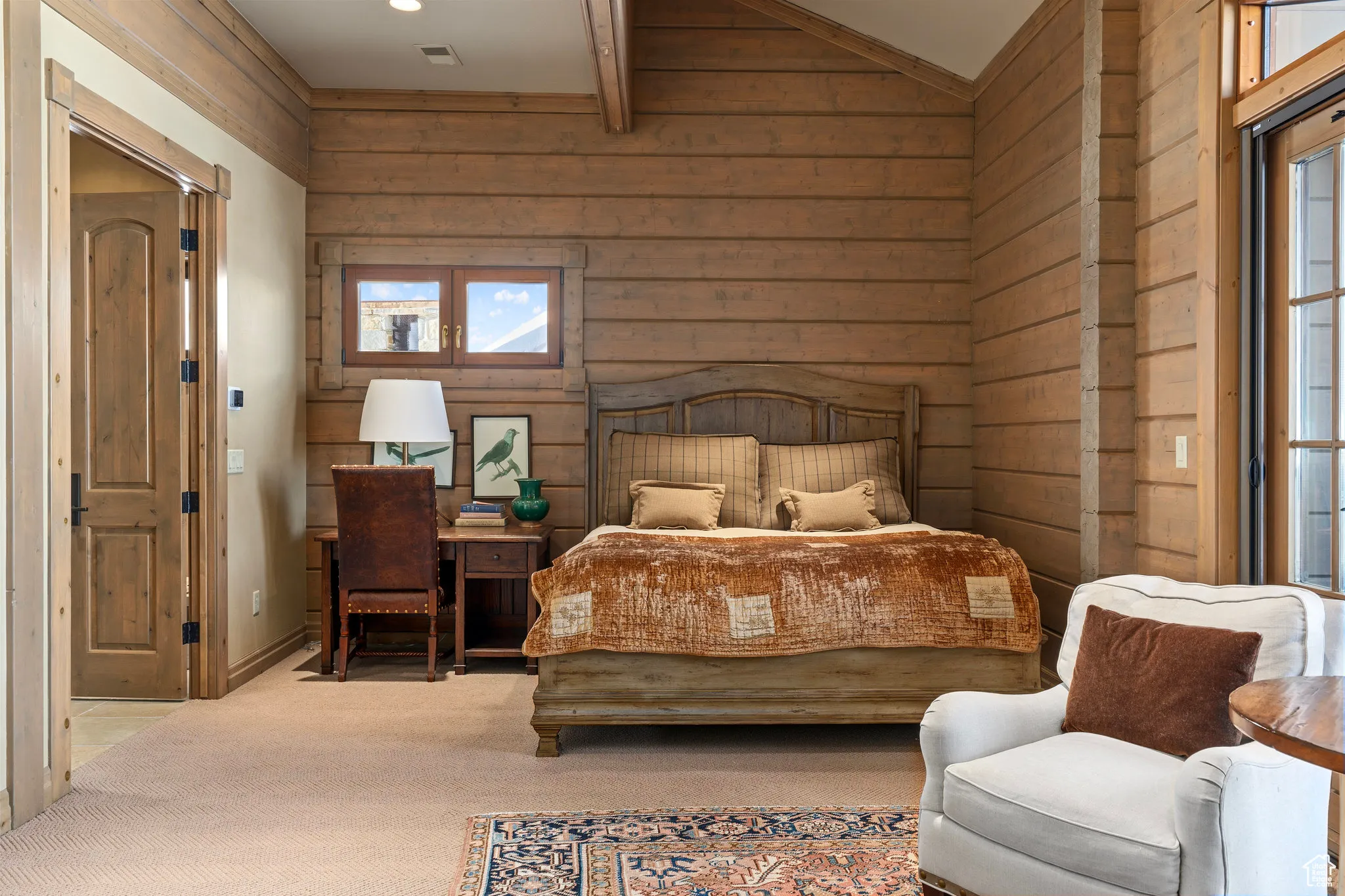 Carpeted bedroom featuring lofted ceiling, wooden walls, and visible vents