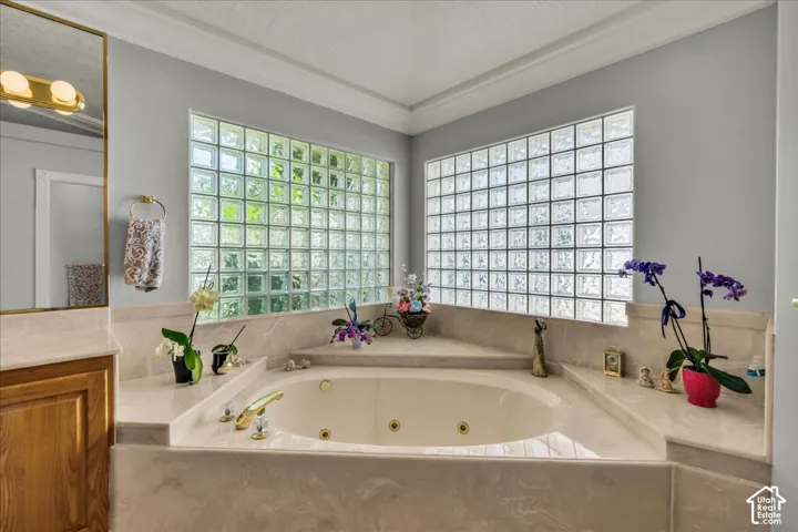 Spacious corner jetted tub featuring a light-toned surround and polished gold-tone fixtures