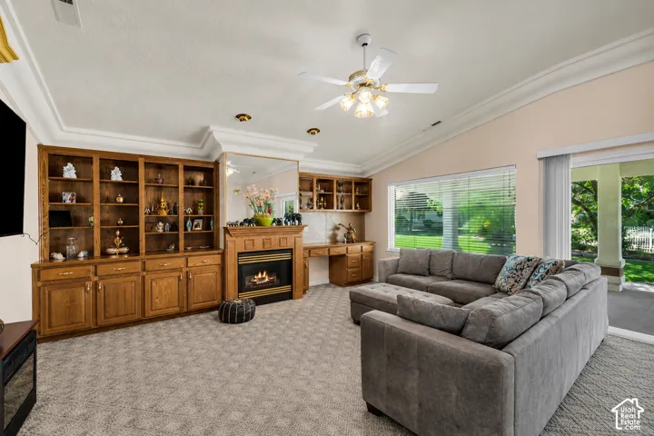 Vaulted ceiling living area featuring a built-in wood cabinetry wall, gas fireplace with wood mantel, ceiling fan, and large windows with horizontal blinds