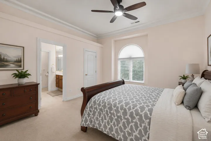 Carpeted bedroom featuring a ceiling fan with integrated lighting, crown molding, arched window with horizontal blinds, and an attached bathroom with a wood-finish vanity