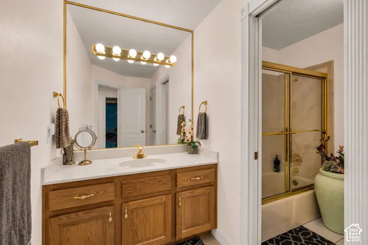 Bathroom vanity featuring a light wood-finish cabinet with gold-tone hardware, a white countertop, and a large mirror with a gold-tone frame