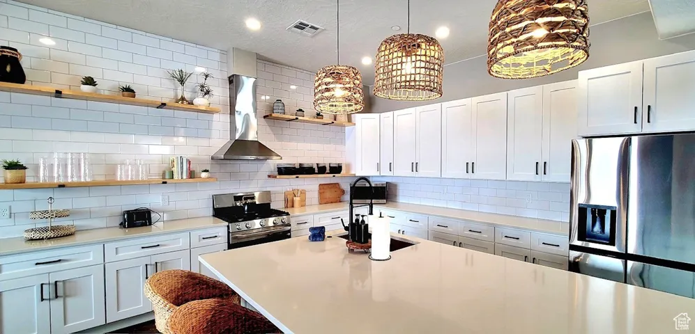 Kitchen featuring stainless steel appliances, visible vents, wall chimney range hood, open shelves, and tasteful backsplash