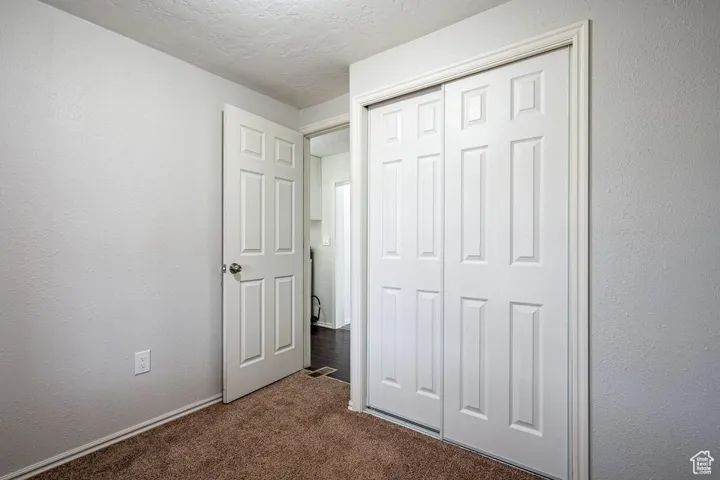 Unfurnished bedroom with carpet floors, a closet, a textured ceiling, and a textured wall